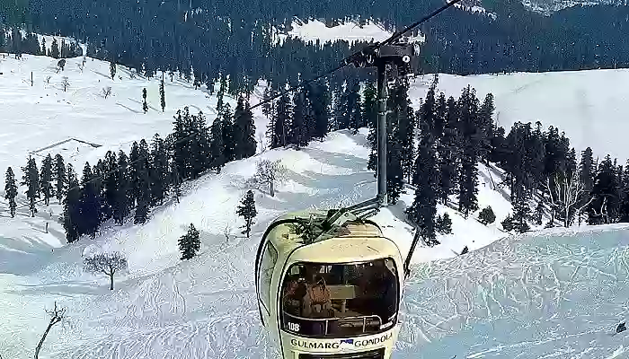 Travelers riding a cable car over a valley covered in snow in Gulmarg